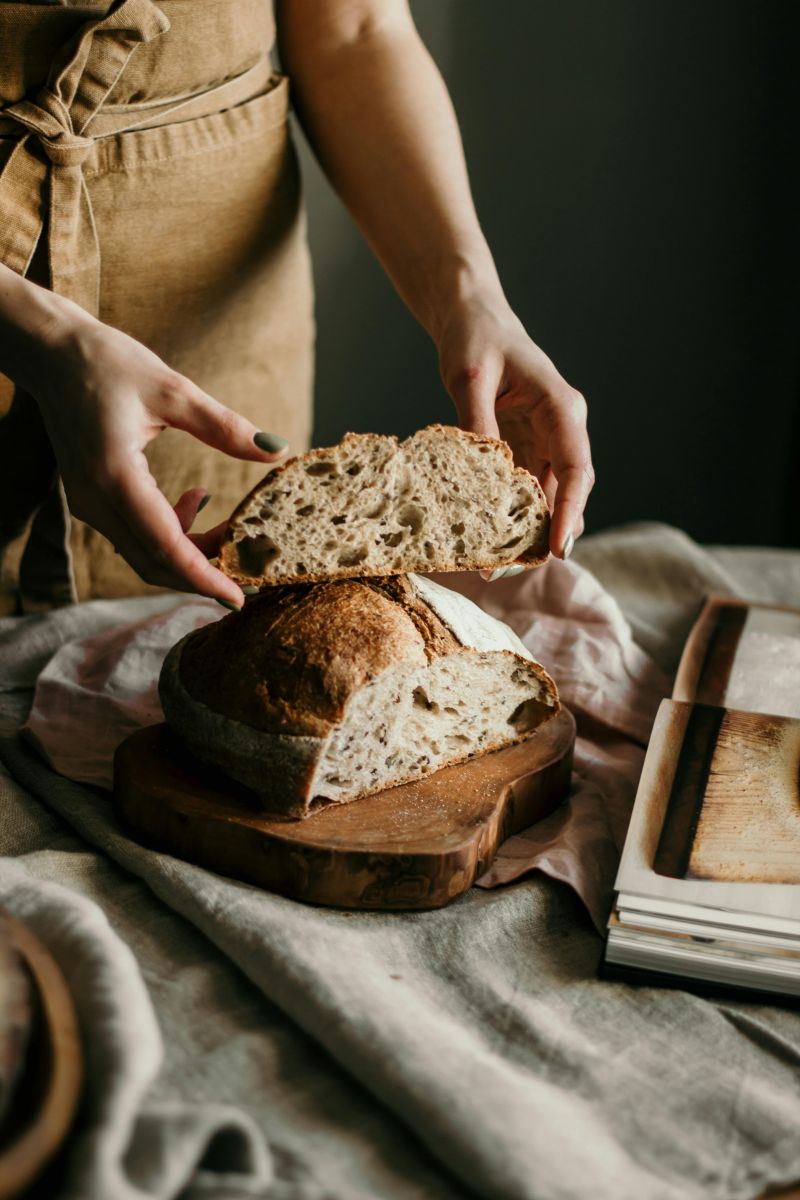 A person holds a slice of sourdough bread, while the rest of the loaf rests on a cutting board.