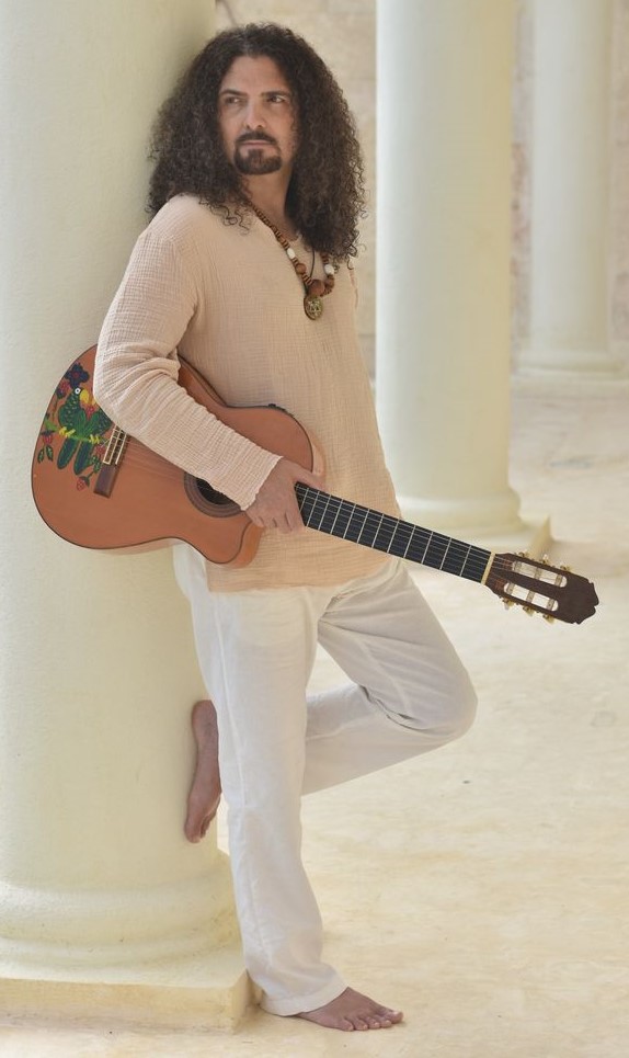 A man leans against a pillar, holding a guitar